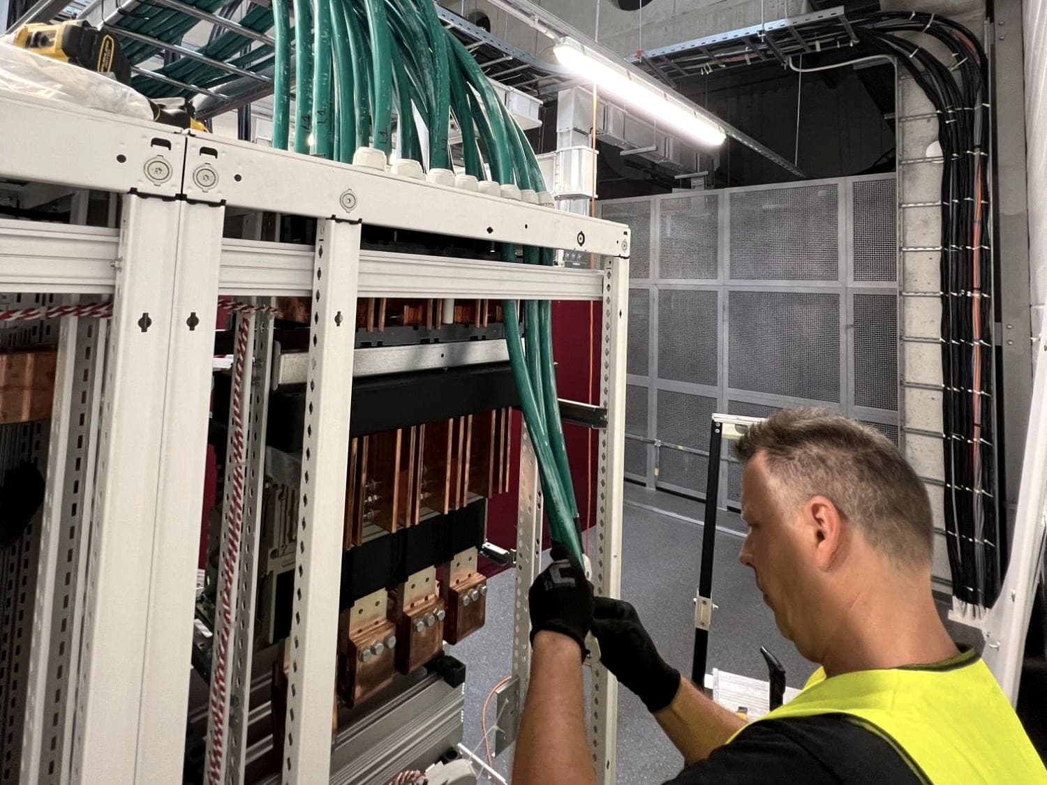 Elektrikár zapája silové káble do hlavného rozvádzača NN s medenými prípojnicami